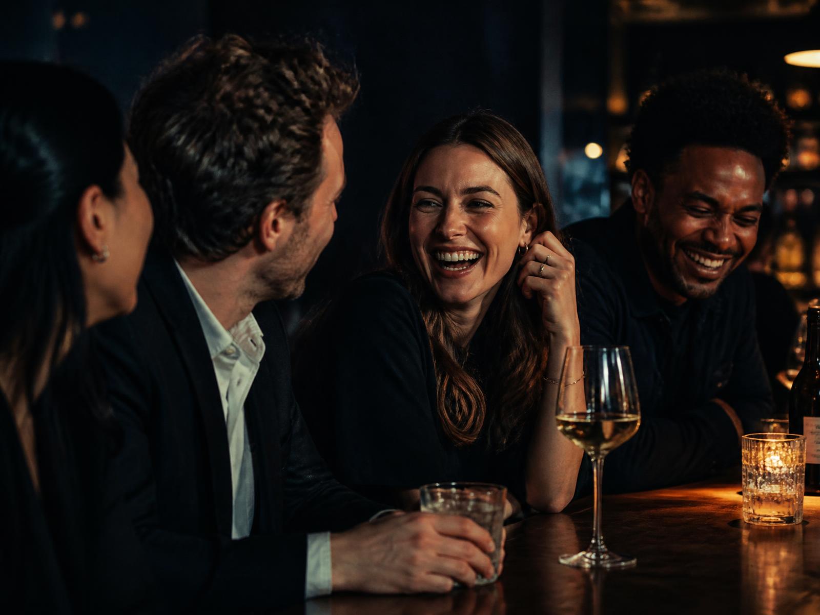 Colleagues laughing over drinks at a bar after work